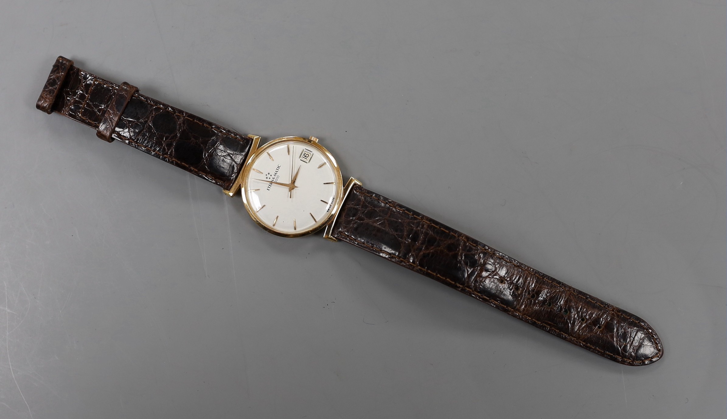 A gentleman's yellow metal Eterna-Matic wrist watch, with date aperture, on associated leather strap (lacking buckle), with baton numerals.
